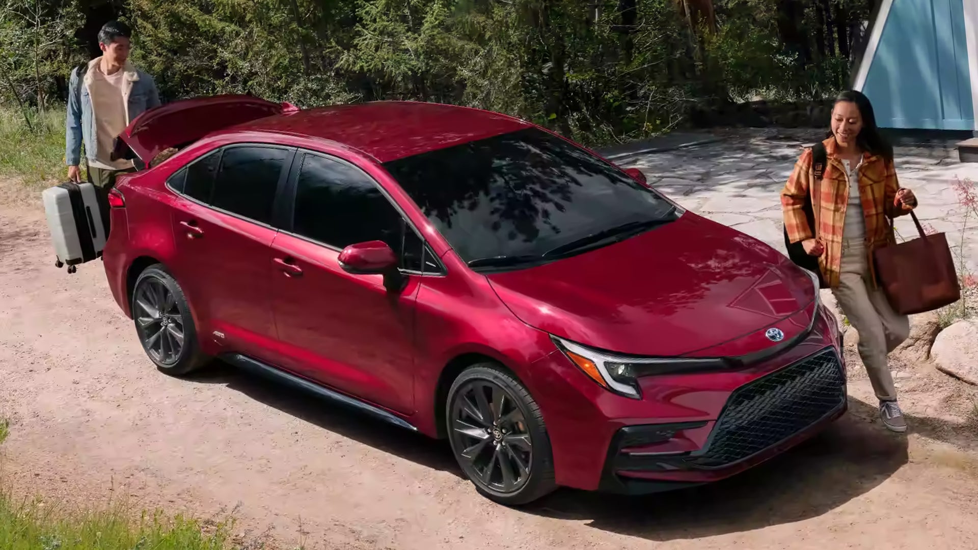 Two people walking around a red Toyota Corolla parked outside